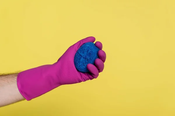 Visão parcial do homem em luva de borracha segurando esfregador prato azul isolado no amarelo — Fotografia de Stock