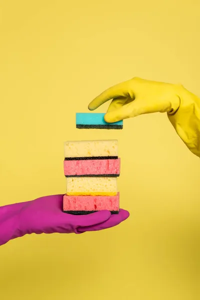 Partial view of woman in rubber glove holding stack of sponges near man isolated on yellow — Stock Photo