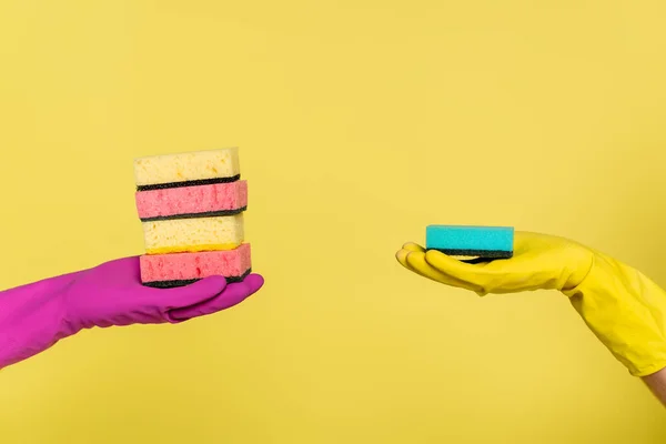 Teilansicht von Frau und Mann in Gummihandschuhen, die Schwämme isoliert auf gelb halten — Stockfoto