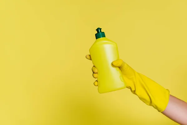 Partial view of cleaner in rubber glove holding bottle with detergent on yellow — Stock Photo