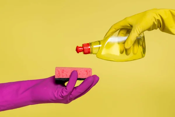 Vue recadrée des personnes en gants de caoutchouc tenant bouteille avec détergent et éponge isolé sur jaune — Photo de stock