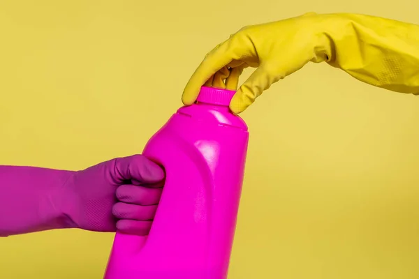 Vue recadrée des personnes en gants de caoutchouc tenant bouteille avec détergent isolé sur jaune — Photo de stock