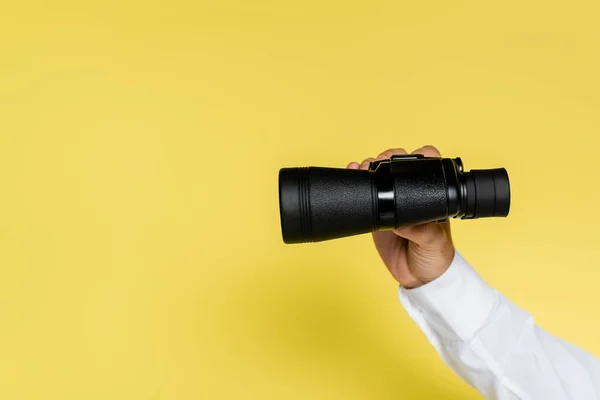 Cropped view of man holding black binoculars on yellow — Stock Photo