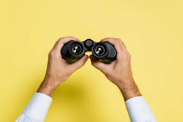 Vista recortada del hombre sosteniendo binoculares negros en las manos en amarillo — Stock Photo