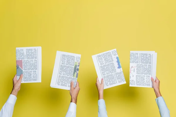 Cropped view of man and woman holding newspapers on yellow — Stock Photo