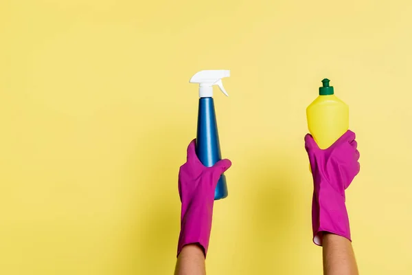 Частковий вид очищувача в гумових рукавичках, що тримає пральний порошок і пляшку розпилювача на жовтому — стокове фото