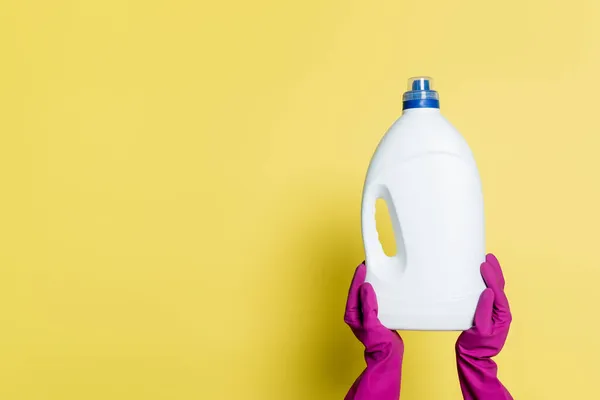 Partial view of cleaner in rubber gloves holding bottle with detergent on yellow — Stock Photo