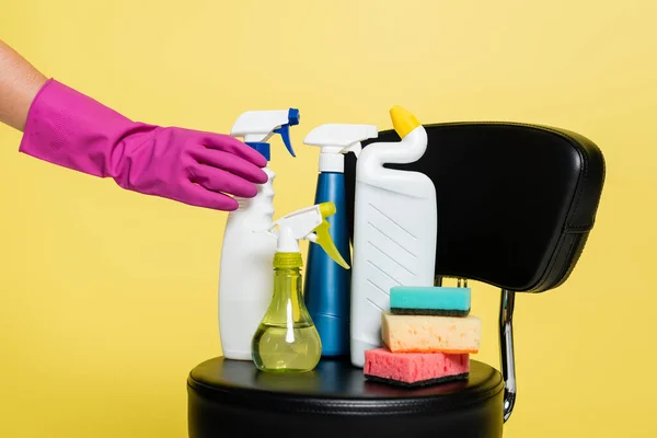 Cropped view of cleaner reaching bottle with detergent near clean sponges on black chair isolated on yellow — Stock Photo