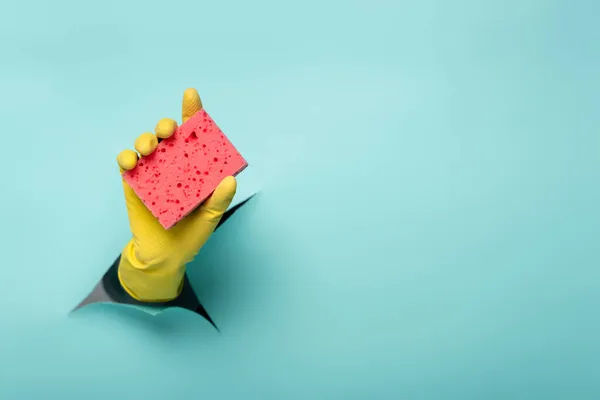 Partial view of cleaner in rubber glove holding sponge through hole in paper wall on blue — Stock Photo