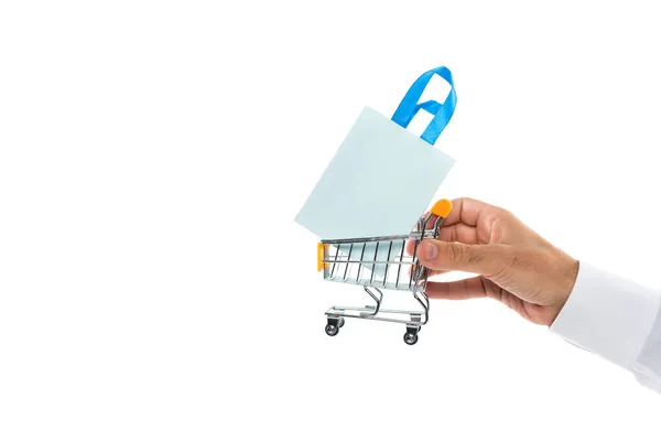 Vista cortada do homem segurando carrinho de compras minúsculo com saco de papel isolado no branco — Fotografia de Stock