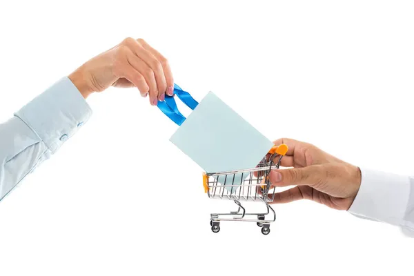 Vista recortada del hombre sosteniendo pequeño carrito de compras cerca de la mujer con bolsa de papel aislado en blanco - foto de stock