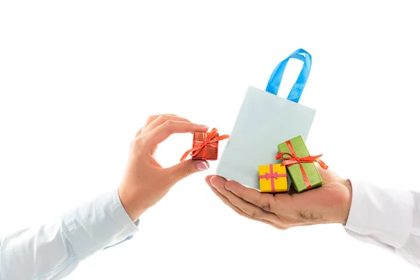 Vista ritagliata dell'uomo che tiene la borsa della spesa vicino alla mano femminile con una piccola scatola regalo isolata sul bianco — Foto stock