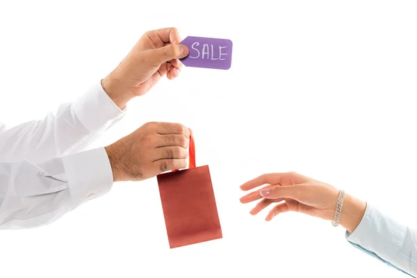 Vista recortada del hombre sosteniendo bolsa de compras y etiqueta de precio cerca de mano femenina aislada en blanco - foto de stock