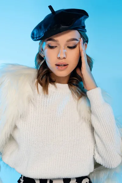 Jeune femme en béret, veste en fausse fourrure et pull blanc posant isolé sur bleu — Photo de stock