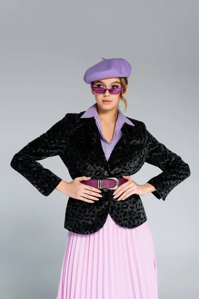 Stylish young woman in beret and blazer with animal print posing with hands on hips isolated on grey — Stock Photo