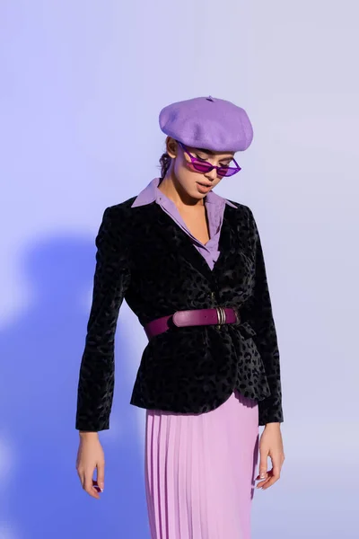 Trendfrau in Baskenmütze, Sonnenbrille und Blazer mit Animal Print posiert auf Violett — Stockfoto