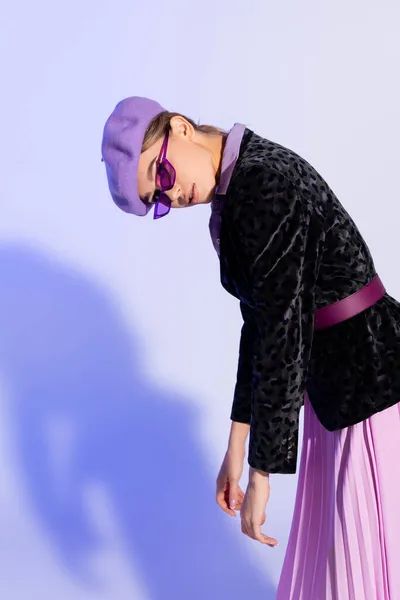 Trendy woman in beret, sunglasses and blazer with animal print looking at camera on purple — Stock Photo