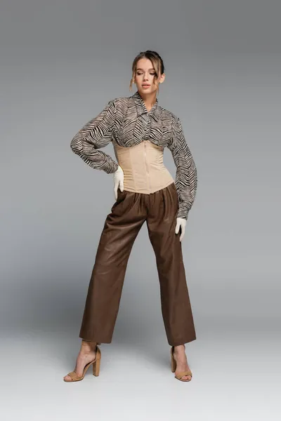 Piena lunghezza di donna alla moda in camicetta con stampa zebra in posa con mano sul fianco su grigio — Foto stock