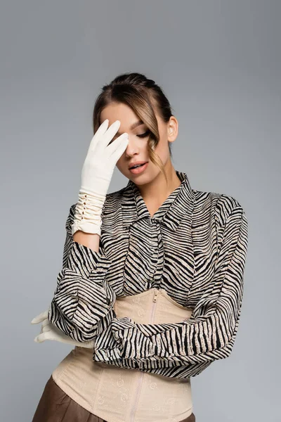 Bonita mujer en blusa con estampado animal y guantes blancos posando aislada sobre gris - foto de stock