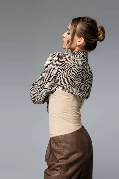 Mujer joven en blusa con estampado animal y corsé beige posando aislada sobre gris - foto de stock