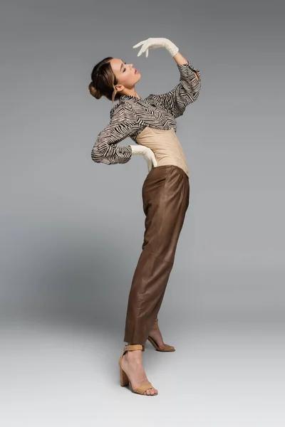 Full length of stylish woman in blouse with zebra print posing with hand on hip while bending on grey — Stock Photo