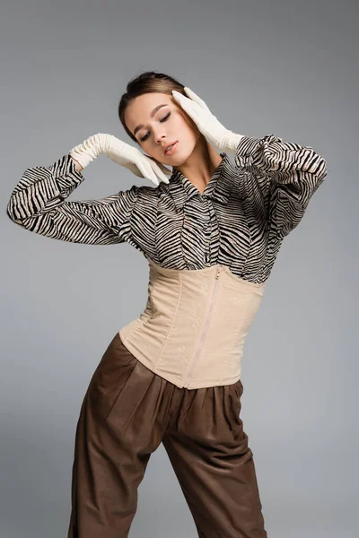 Trendy woman in blouse with animal print, gloves and corset posing isolated on grey — Stock Photo