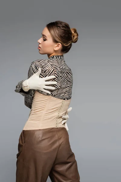 Trendy woman in blouse with animal print, gloves and corset embracing herself isolated on grey — Stock Photo