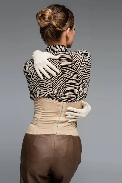 Back view of woman in blouse with animal print, gloves and corset embracing herself isolated on grey — Stock Photo