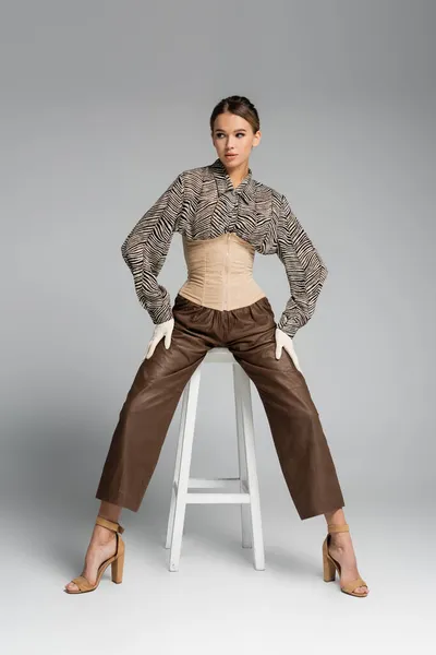 Full length of trendy woman in blouse with zebra print sitting on stool on grey — Stock Photo