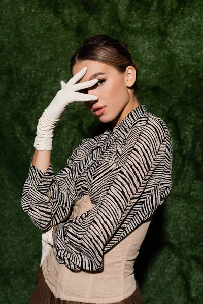 Elegante donna in camicetta con stampa zebra, corsetto e guanti posa vicino sfondo erboso — Foto stock