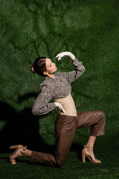 Полная длина стильная женщина в блузке с зеброй отпечаток позирует с рукой на бедре при изгибе возле травянистого фона — стоковое фото
