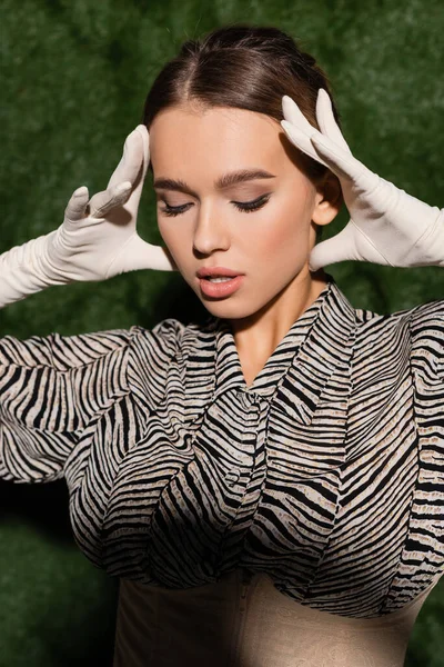 Trendy model in blouse with animal print and gloves posing near grassy background — Stock Photo