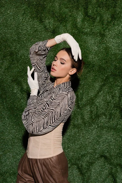 Young woman in blouse with animal print, corset and gloves posing near grassy background — Stock Photo