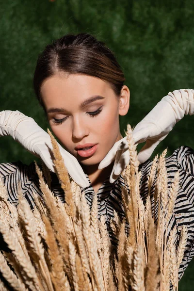 Jeune modèle tendance en chemisier avec imprimé animal et gants blancs posant près des épillets de blé — Photo de stock