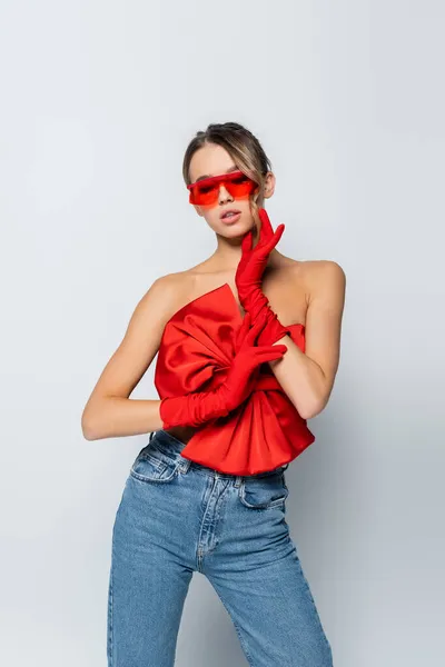 Modèle élégant en chemisier rouge, lunettes de soleil et gants posant isolé sur gris — Photo de stock