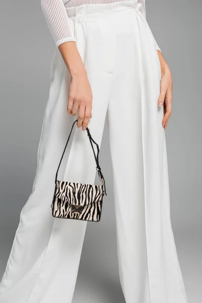 Cropped view of young woman in white pants holding purse with animal print on grey — Stock Photo