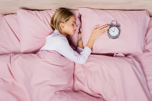 Top view of young woman sleeping near alarm clock on pillow on bed — Stock Photo