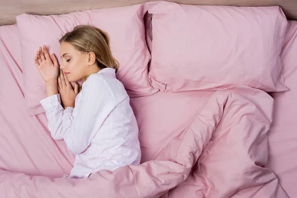 Vista superior de la mujer en pijama durmiendo en ropa de cama rosa en casa - foto de stock