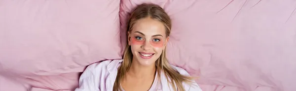 Top view of positive woman with eye patches looking at camera on bed, banner — Stock Photo