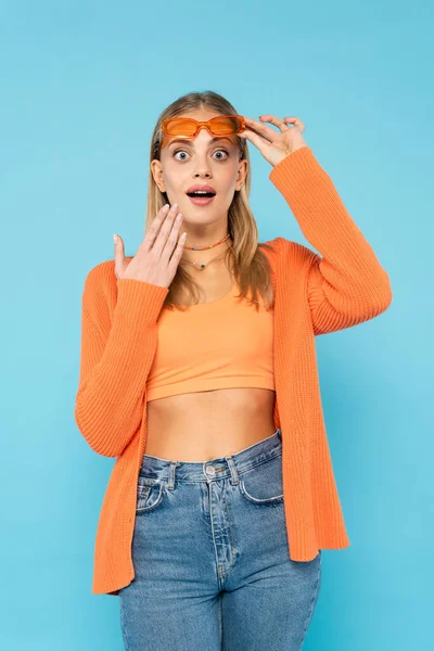 Mujer rubia excitada en gafas de sol mirando a la cámara aislada en azul - foto de stock