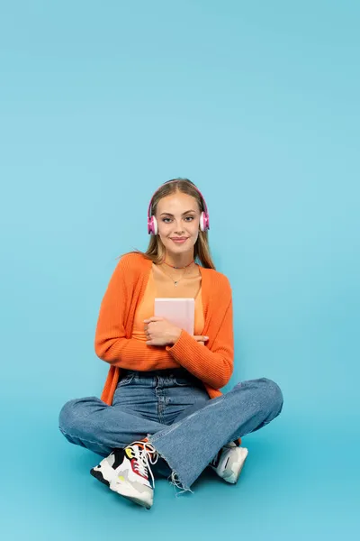 Smiling student in headphones holding notebook on blue background — Stock Photo