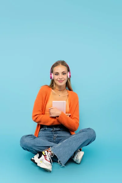 Estudante sorrindo em fones de ouvido segurando notebook no fundo azul — Fotografia de Stock