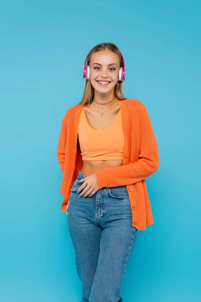 Young woman listening music in headphones and looking at camera isolated on blue — Stock Photo