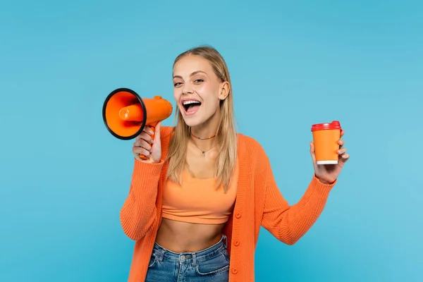 Blonde woman screaming in loudspeaker and holding paper cup isolated on blue — Stock Photo