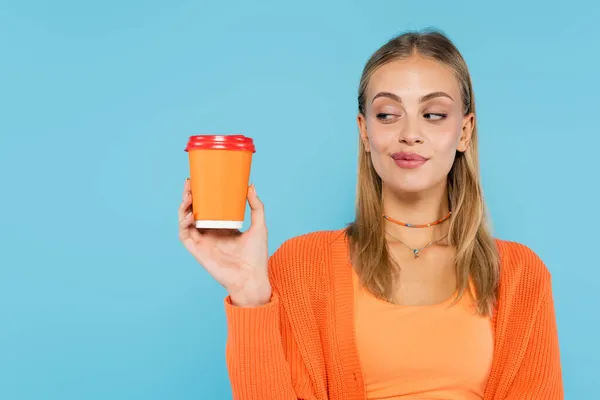 Jovem loira olhando para o café para ir isolado em azul — Fotografia de Stock