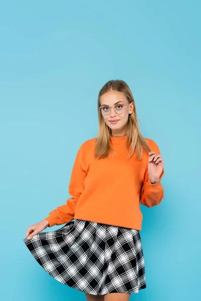 Blonde student holding skirt and looking at camera isolated on blue — Stock Photo