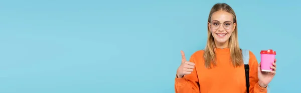 Estudante loira bonita segurando copo de papel e mostrando como gesto isolado em azul, banner — Fotografia de Stock