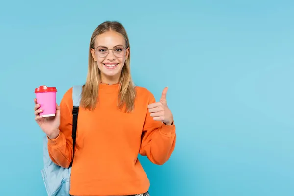 Positive student with backpack and coffee to go showing like gesture isolated on blue — Stock Photo