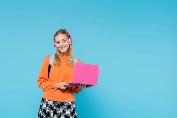 Bella studentessa bionda in cuffie che tiene il computer portatile isolato su blu — Foto stock