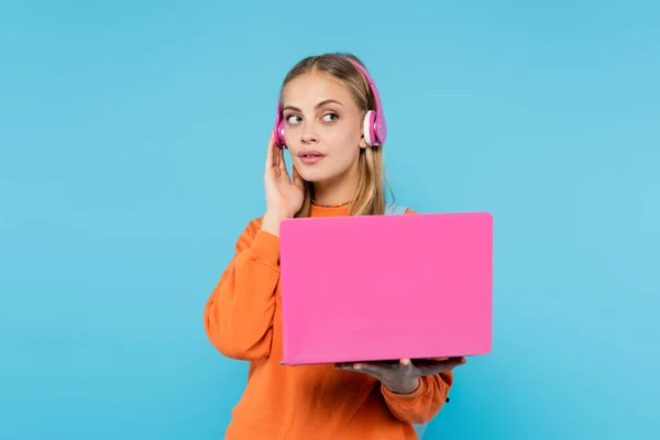 Femme blonde dans les écouteurs tenant ordinateur portable rose isolé sur bleu — Photo de stock